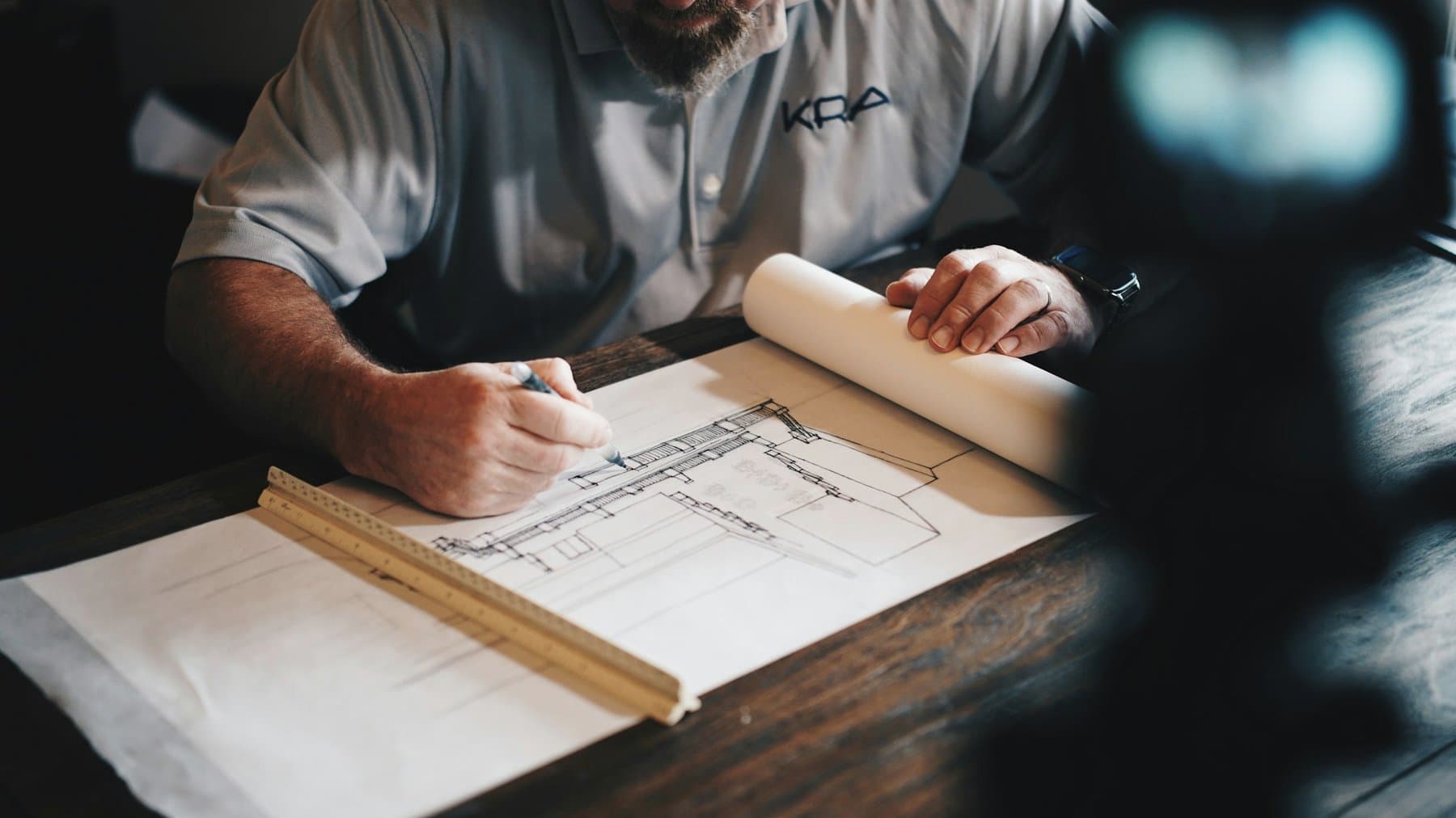 A hand drafting a plan in pencil with a scale ruler on paper