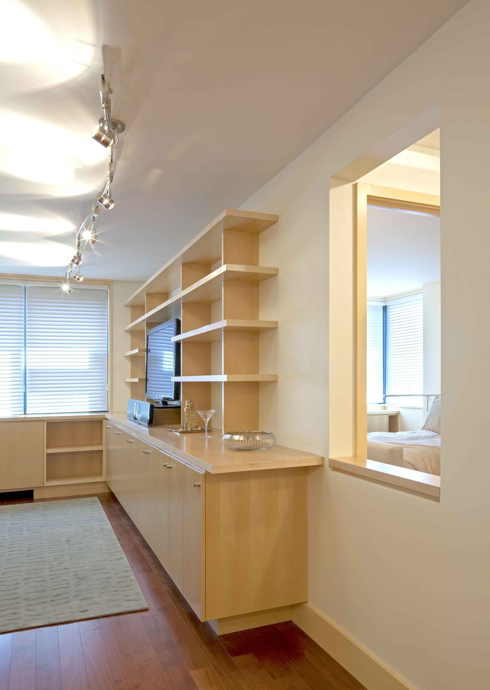 A maple shelving wall in the Baxter Residence with an interior window opening to the bedroom