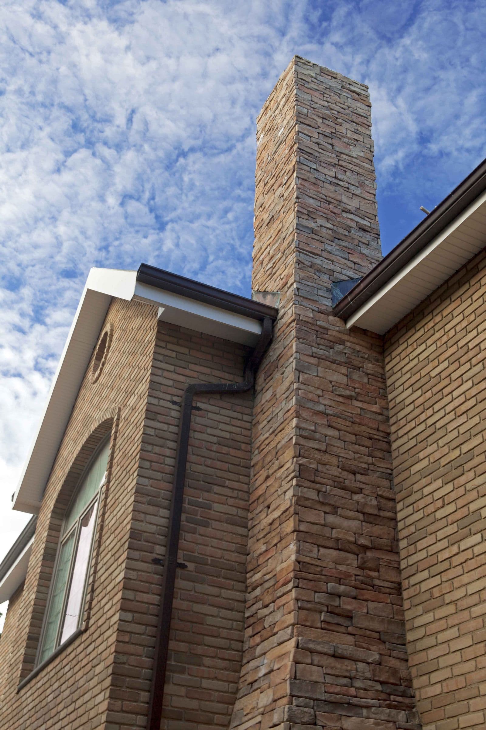 Brick gable and stone chimney detail of the Brión Residence against the sky