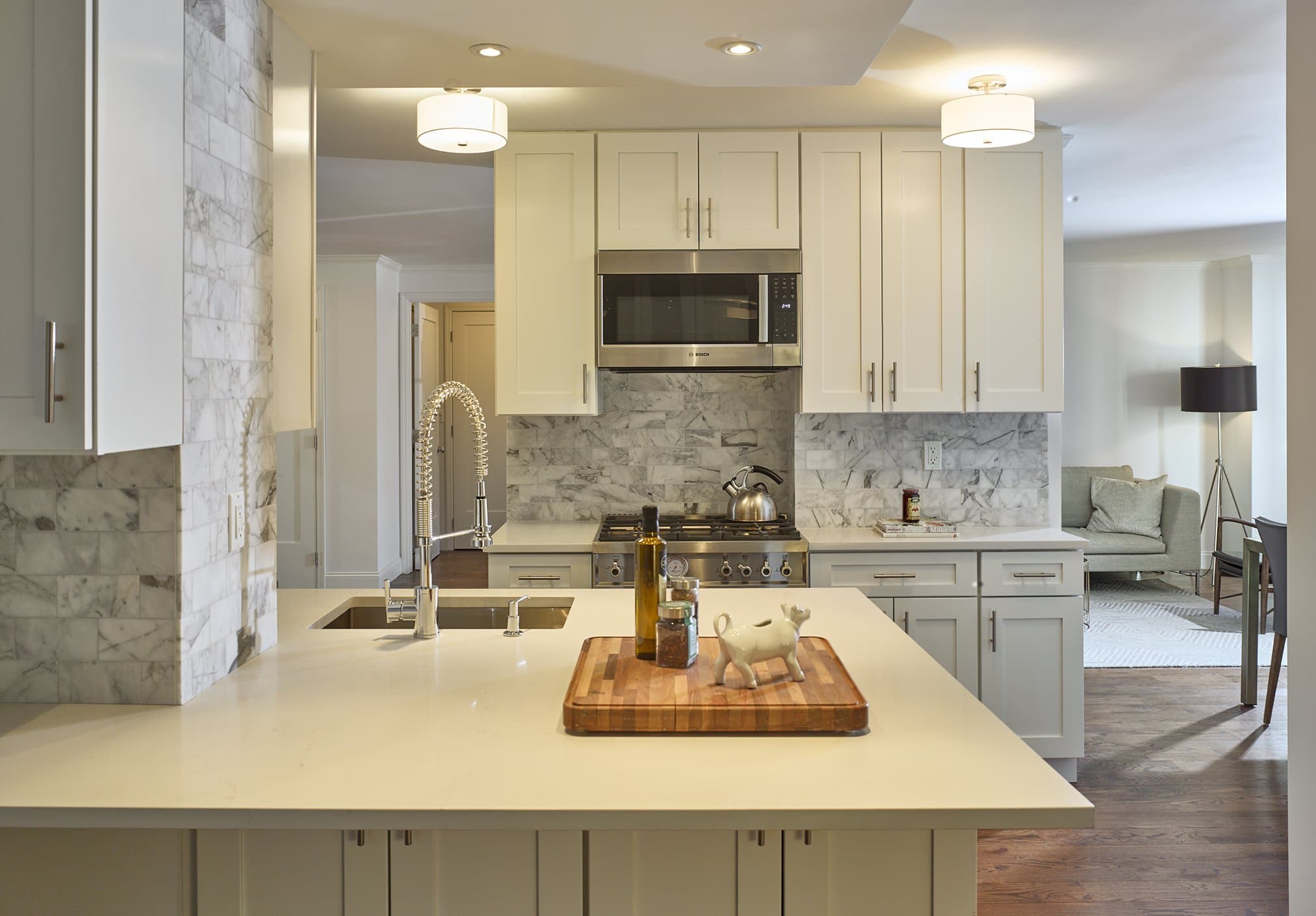 The Greenbaum Residence kitchen, white cabinetry and Carrara marble backsplash opening to the living room